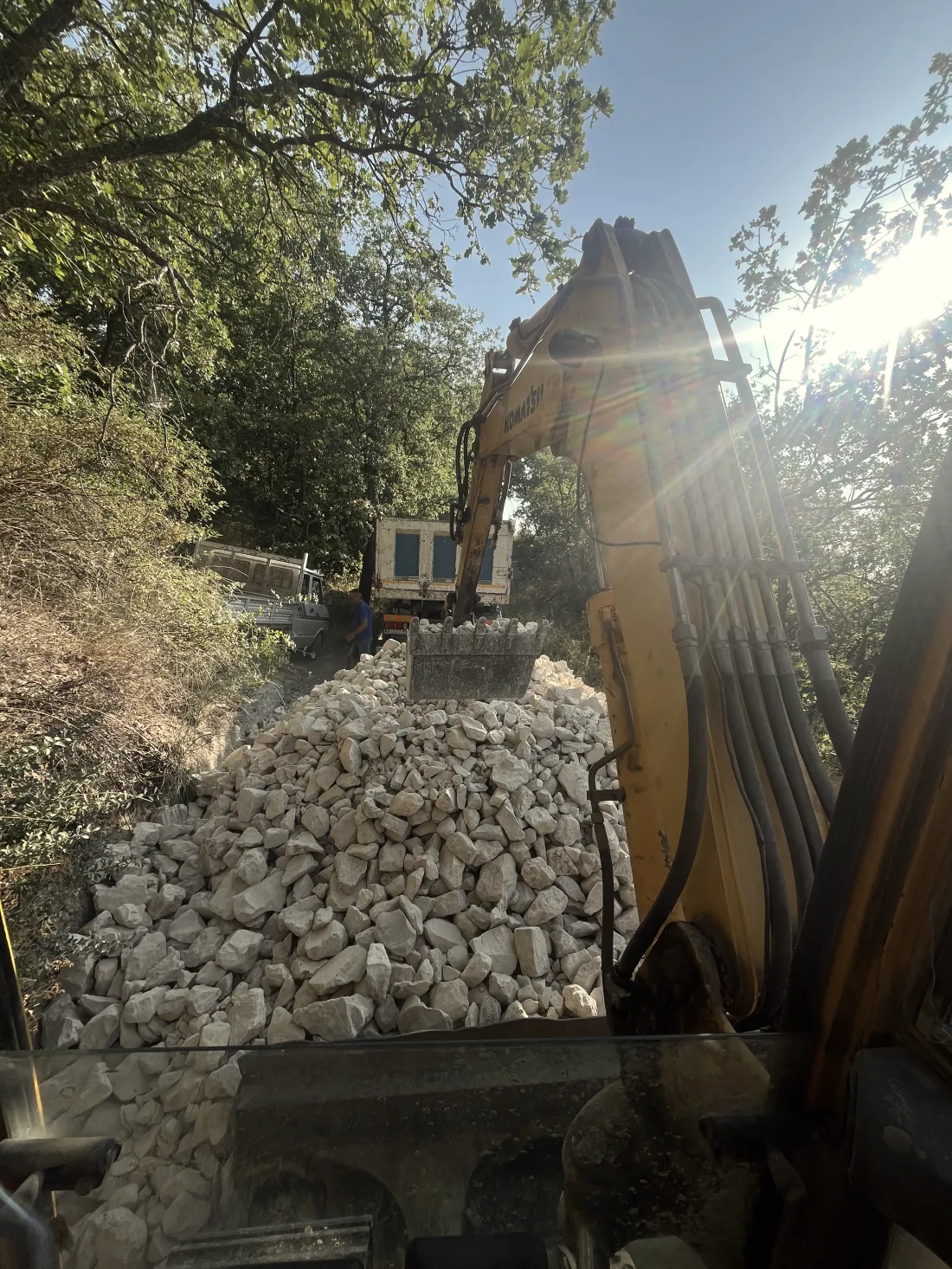 Escavatore che stende pietrame su una pista di accesso nel bosco